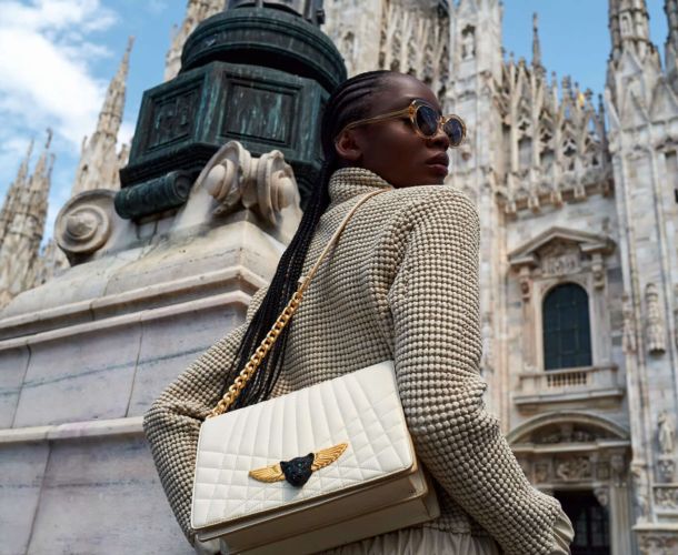 Woman posing stylishly near a historic cathedral with a luxury handbag.