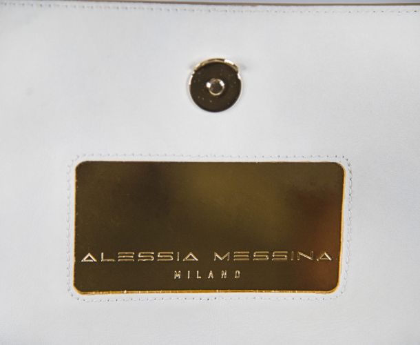 Close-up of a white leather item with a gold label and magnetic snap.