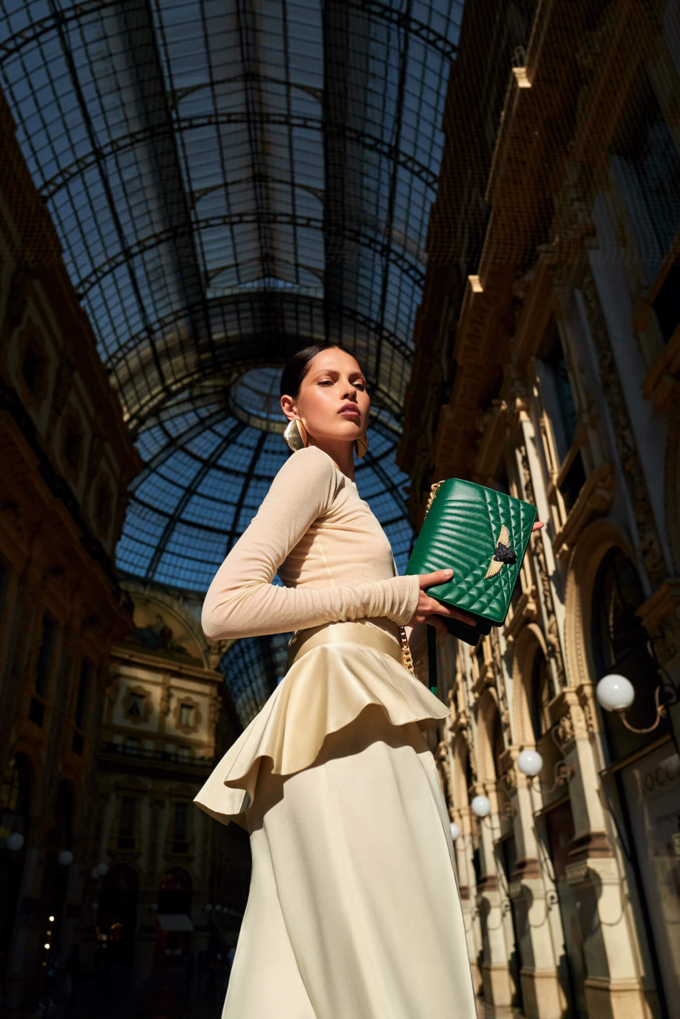 Fashionable woman holding a green clutch in an elegant glass-ceilinged gallery.