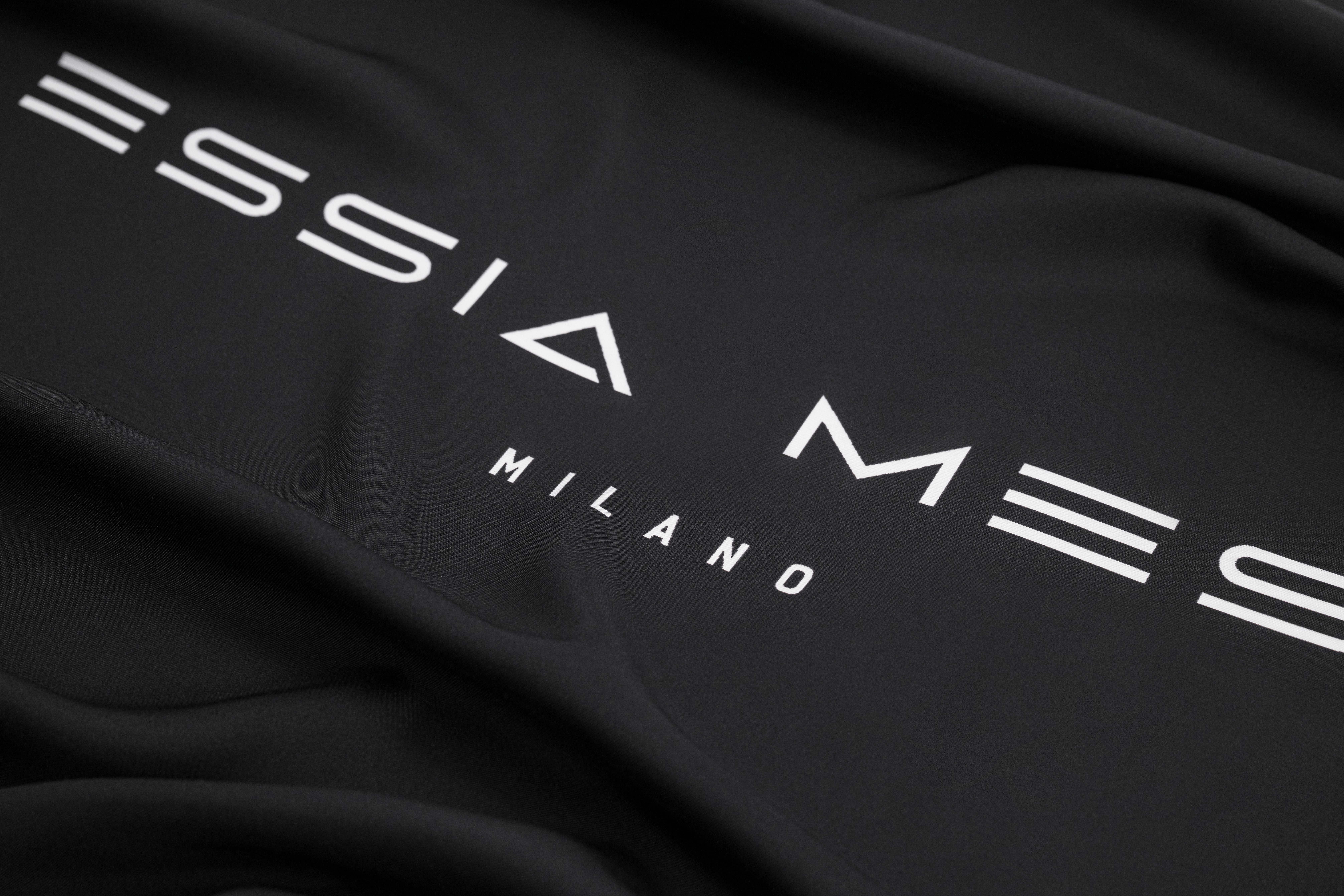 Close-up of black fabric with "Missia Me Milano" text printed in white.