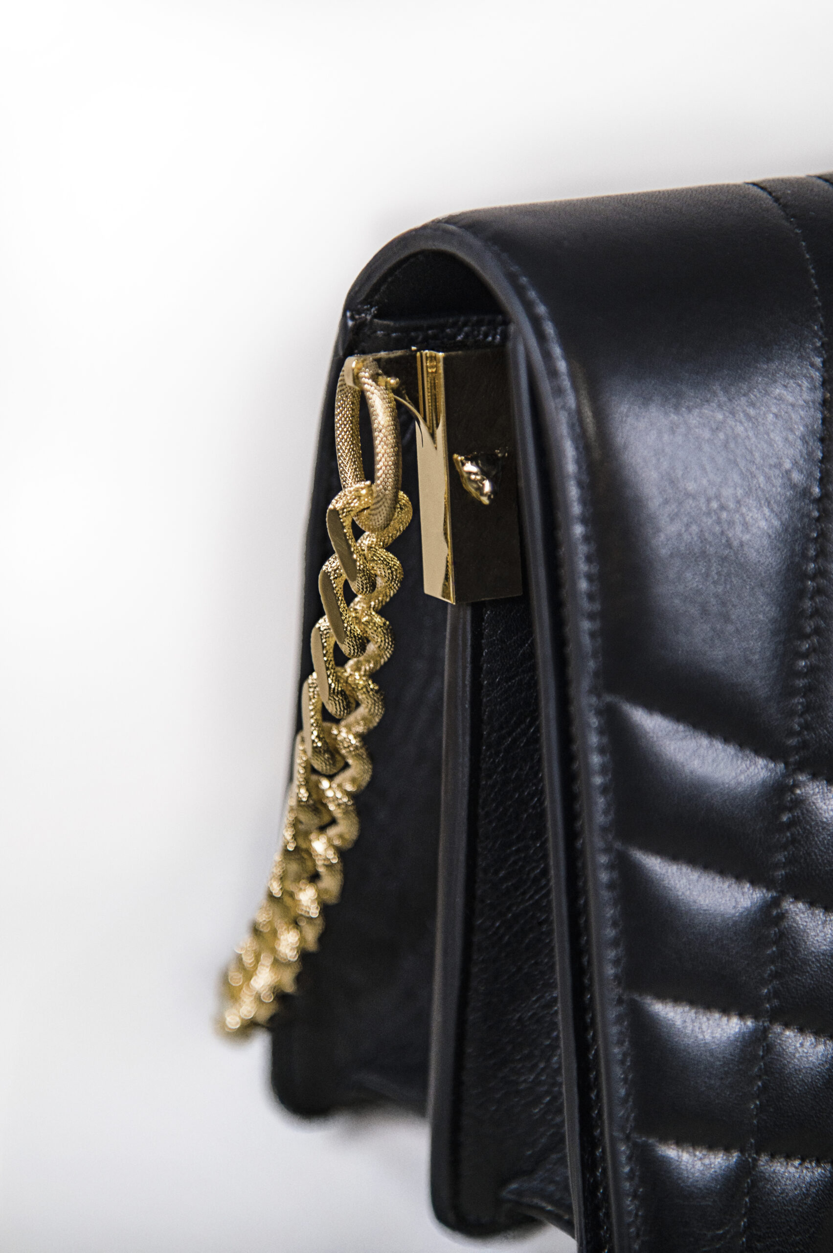 Close-up of a black leather handbag with a gold chain strap detail.
