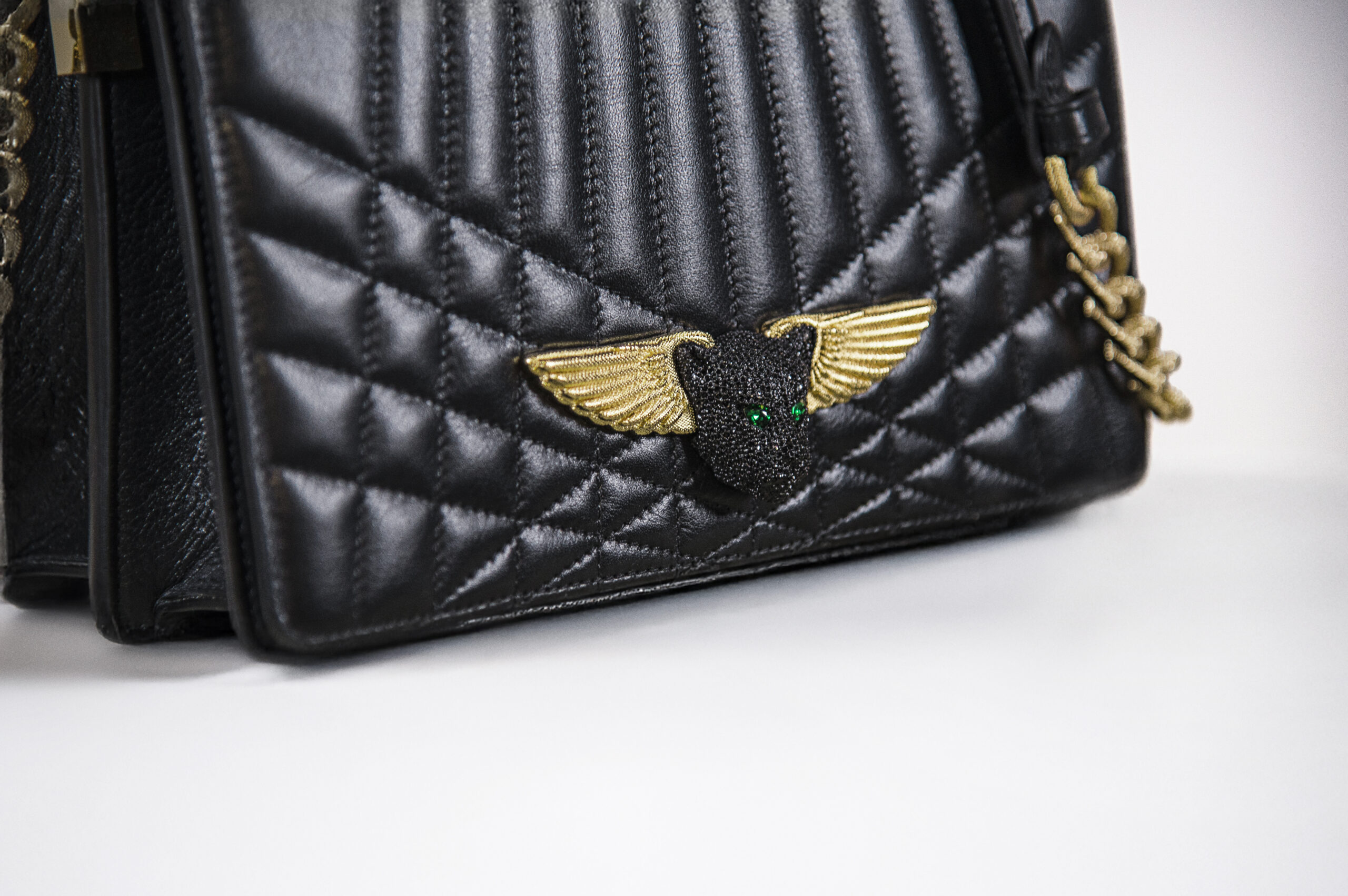 Close-up of a black quilted handbag with a gold winged emblem.