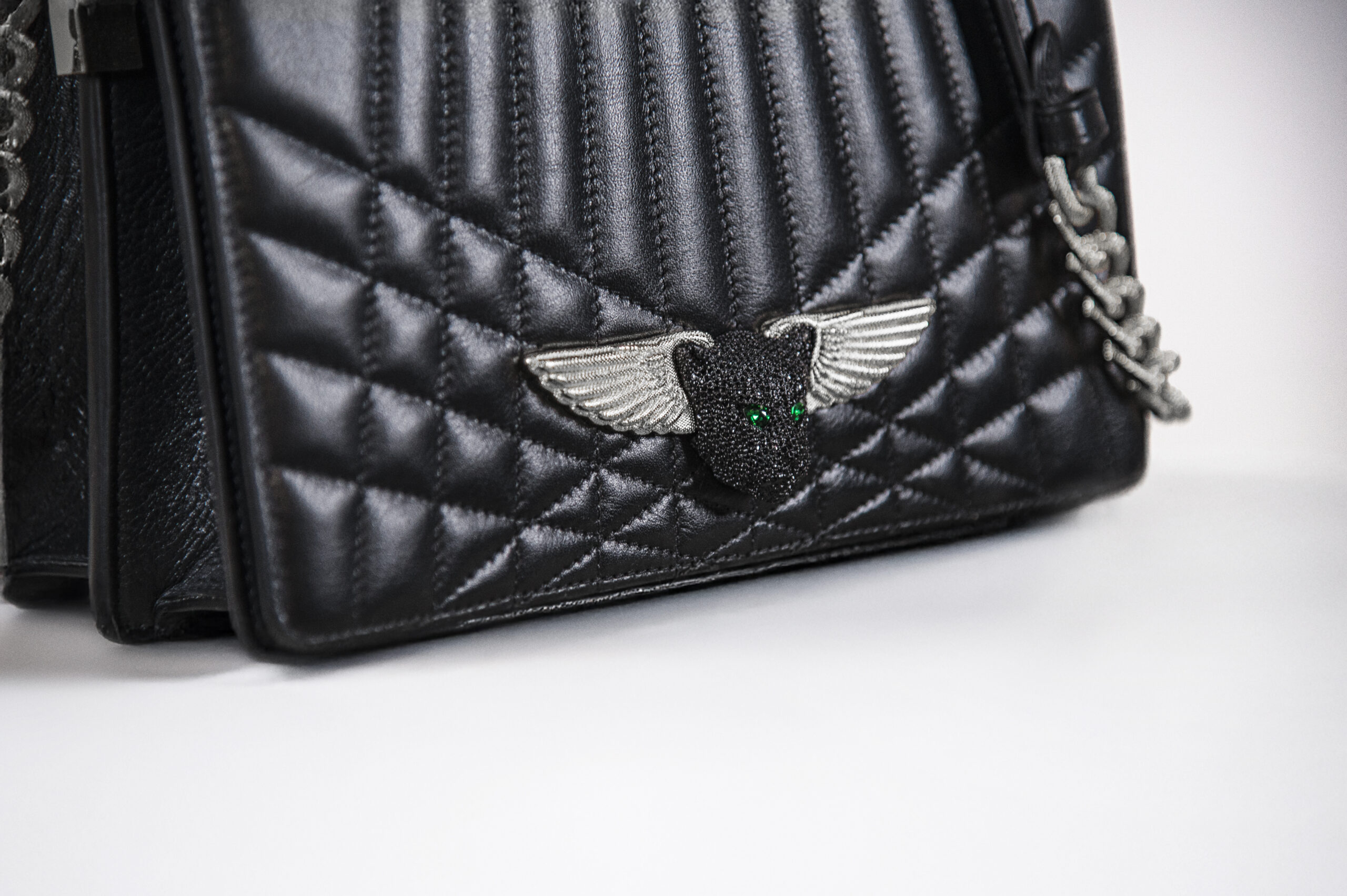 Close-up of a black quilted bag with a winged emblem and green eyes.