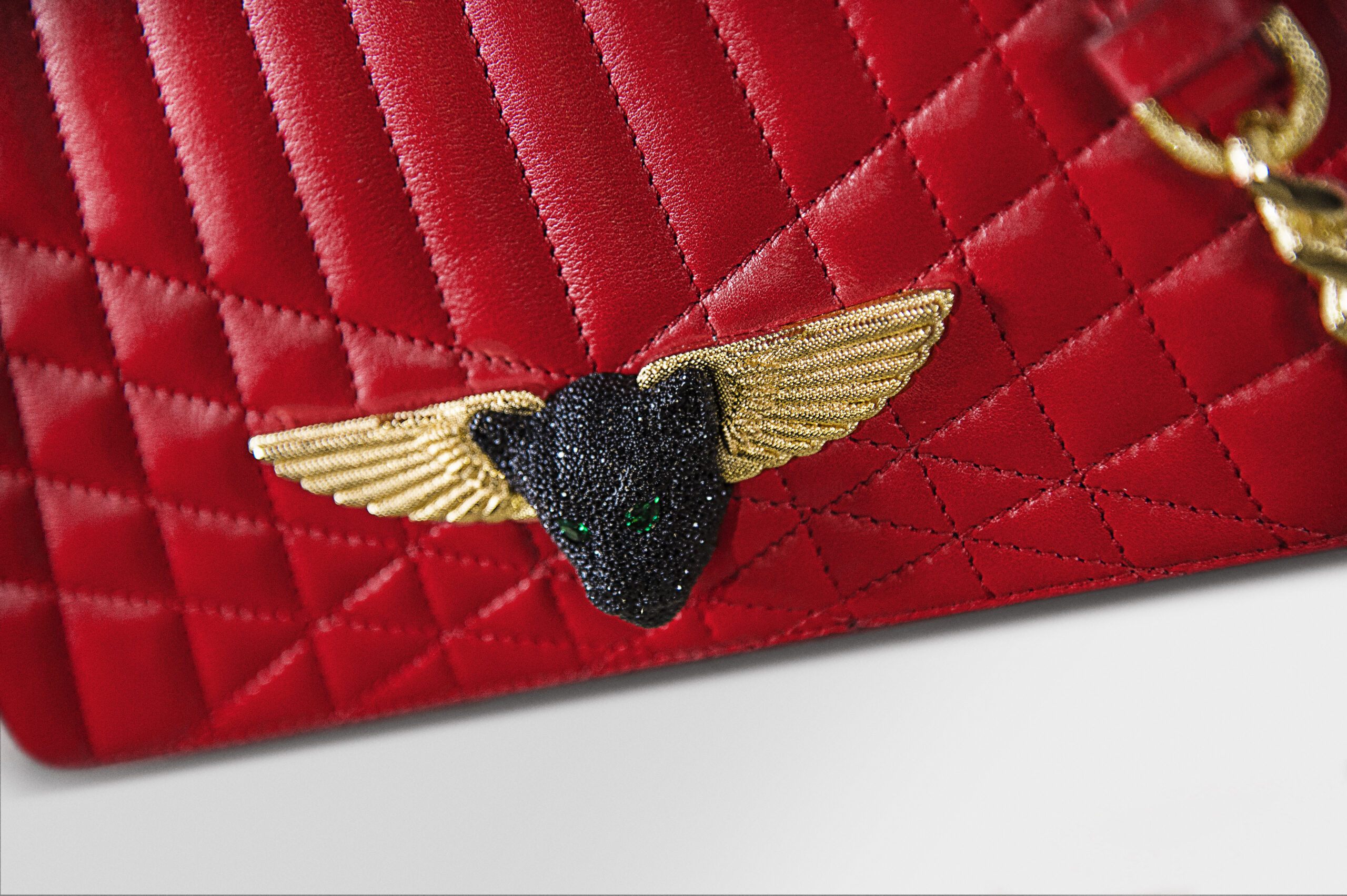 Close-up of a red quilted leather item with a black and gold winged emblem.
