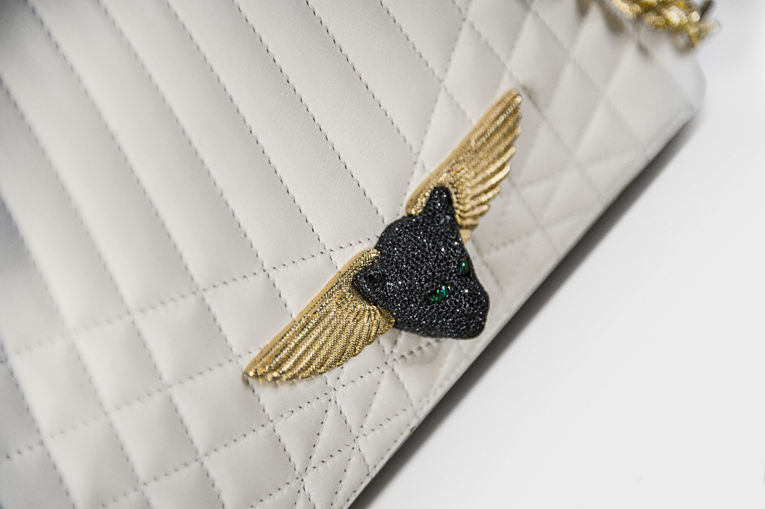 Close-up of a white quilted bag with a black panther and gold wings emblem.