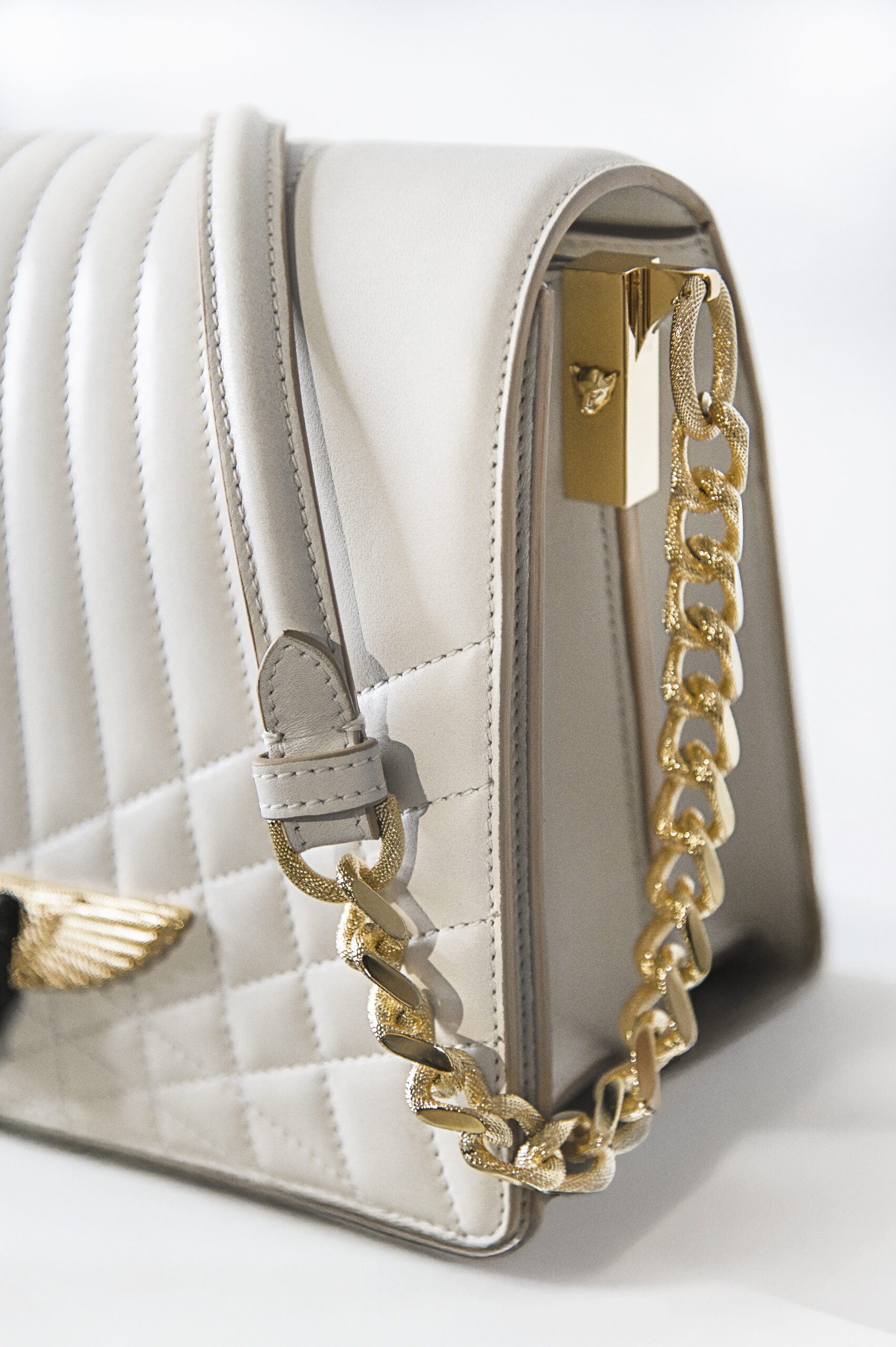 Close-up of a stylish white quilted handbag with gold chain and hardware.