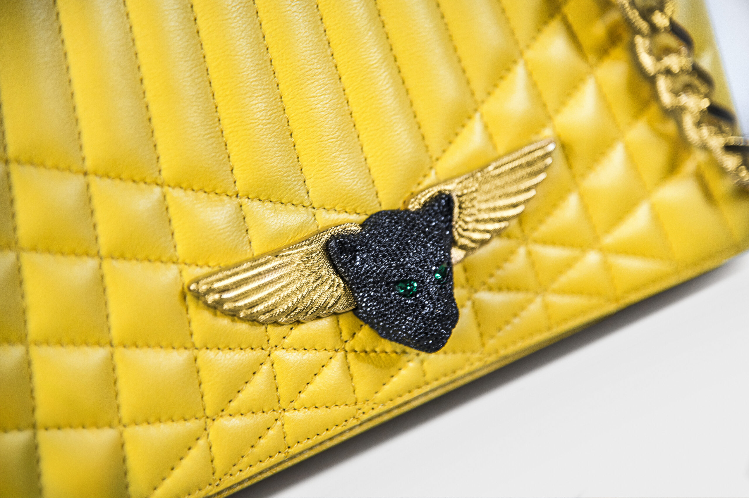 Close-up of a yellow quilted handbag with a bee emblem.