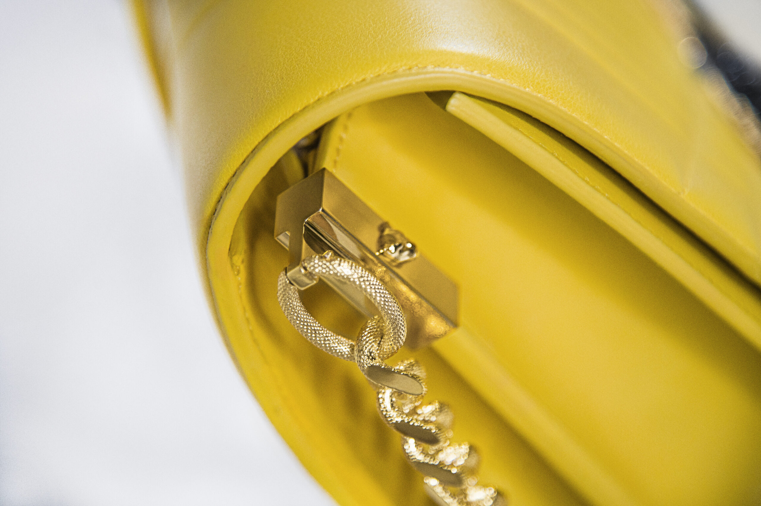 Close-up of a yellow handbag with gold chain and clasp.