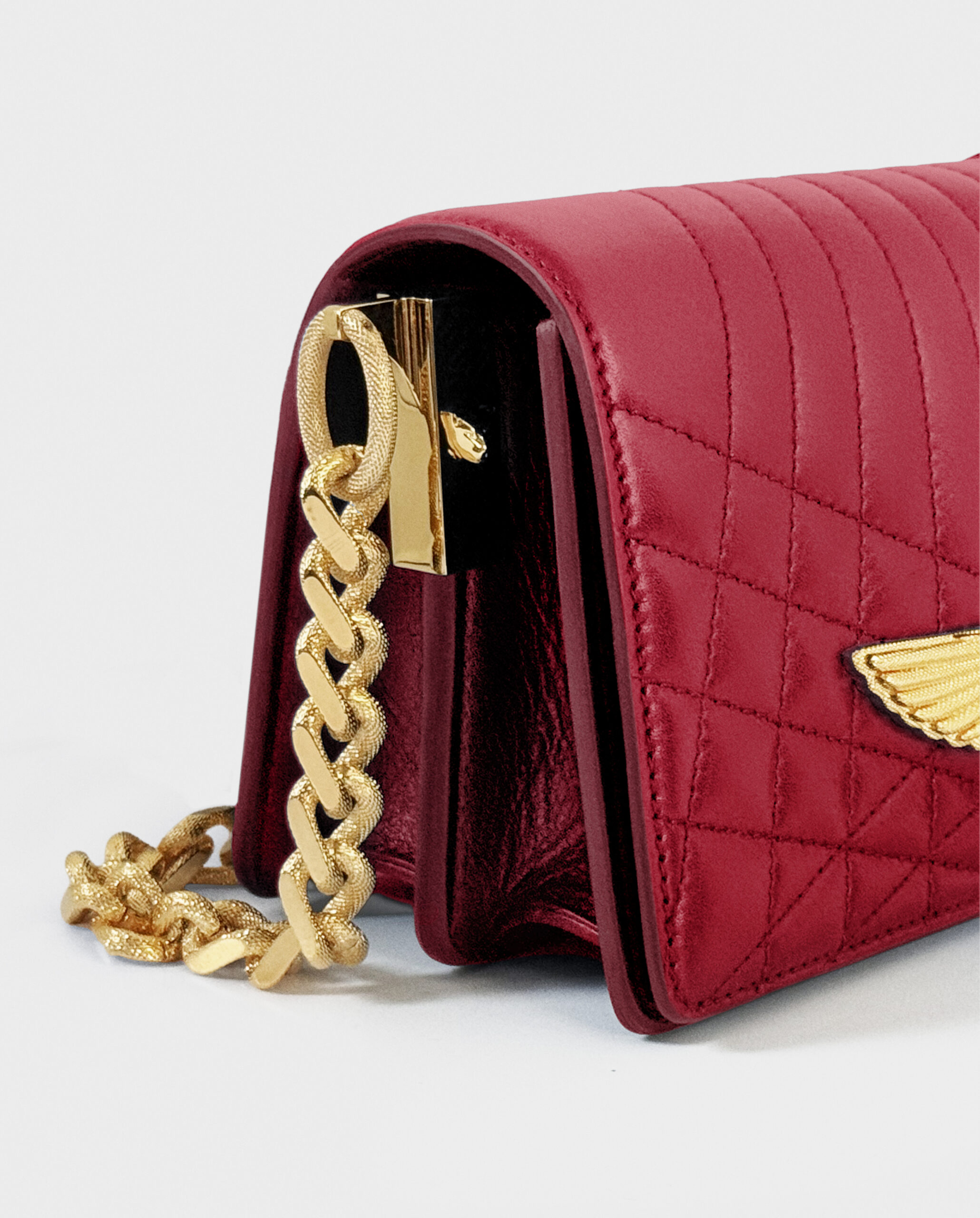 Close-up of a red quilted handbag with a gold chain and winged emblem.