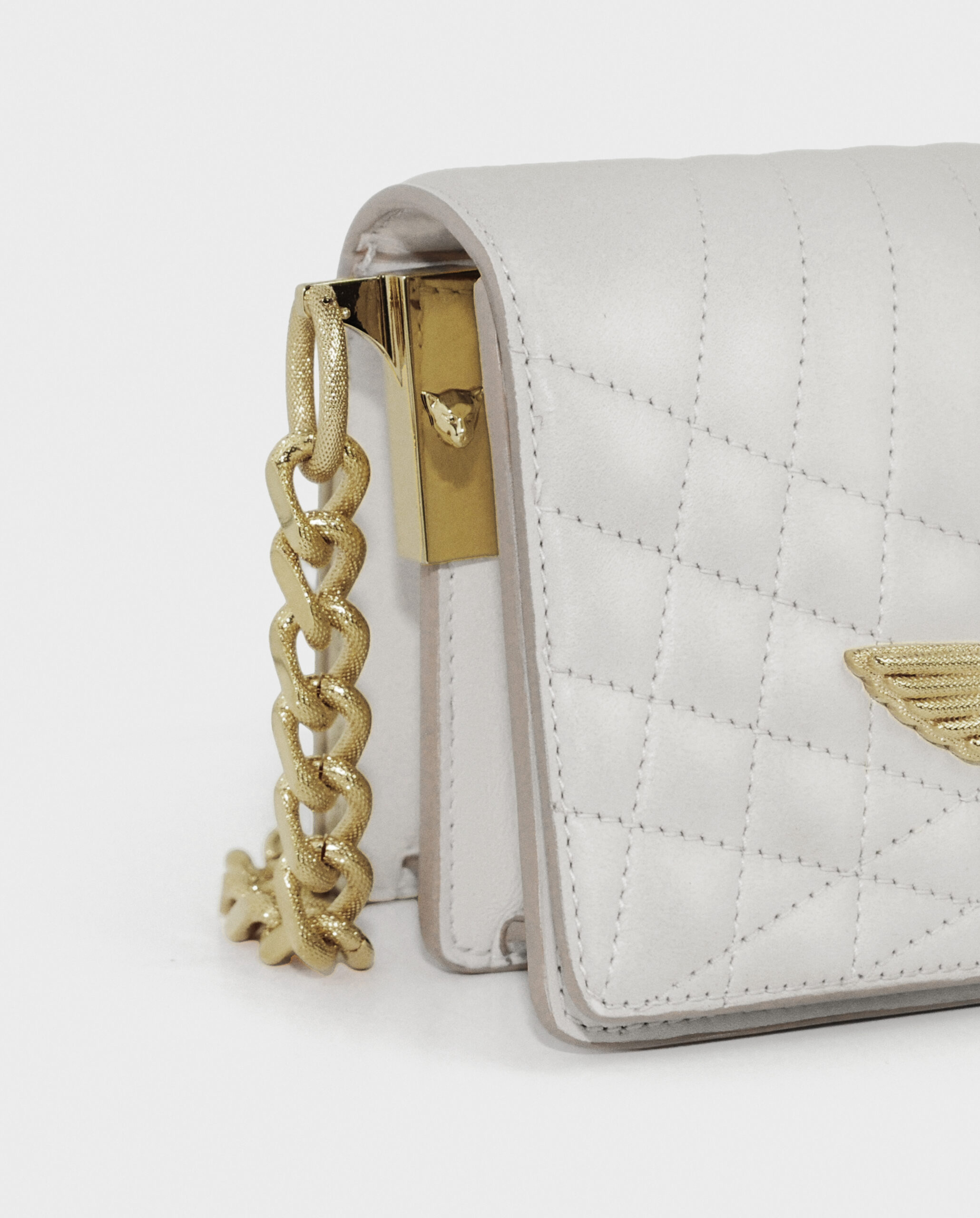 Close-up of a white quilted handbag with a gold chain strap and emblem.