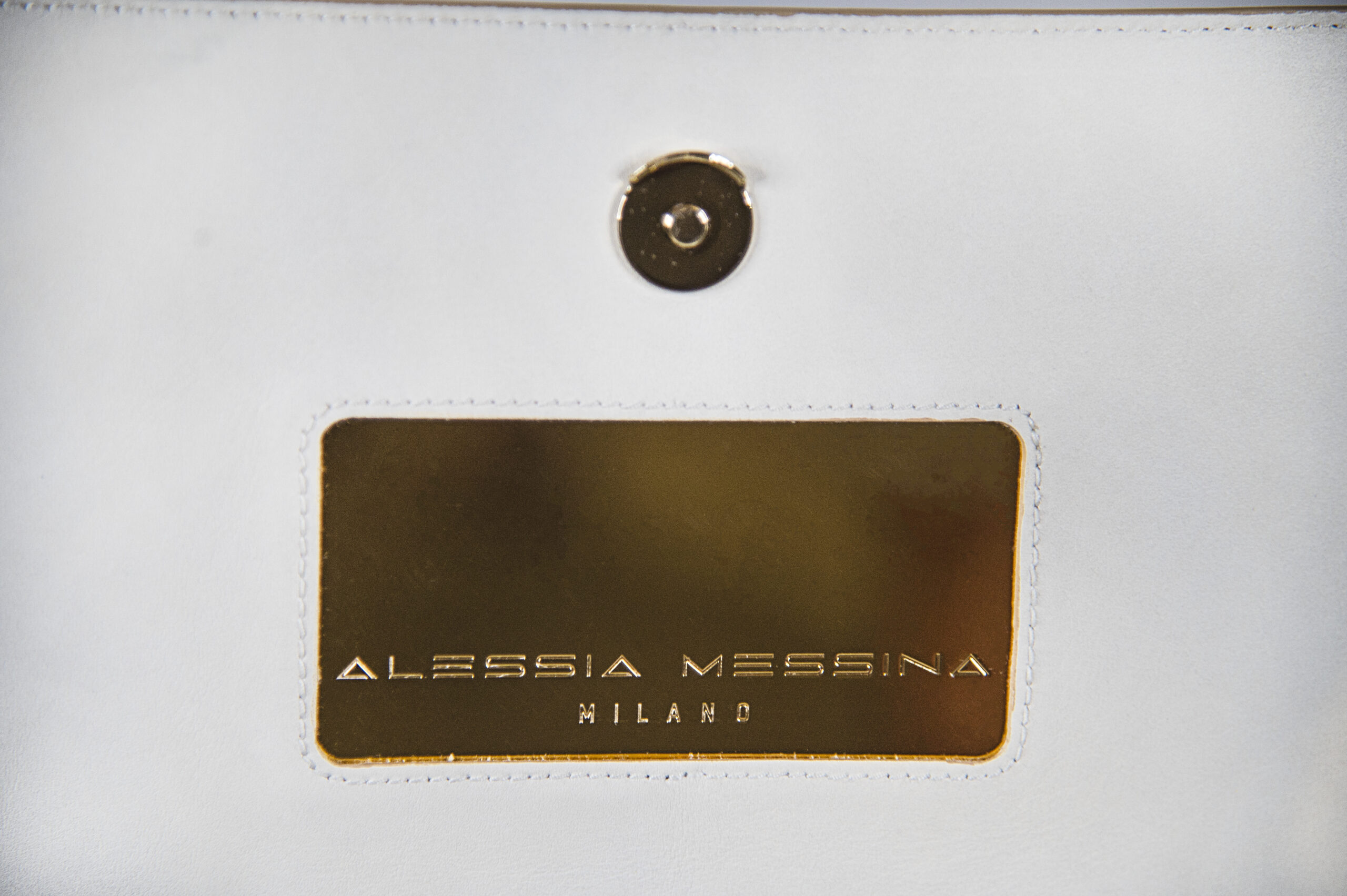 Close-up of a white leather item with a gold label and magnetic snap.