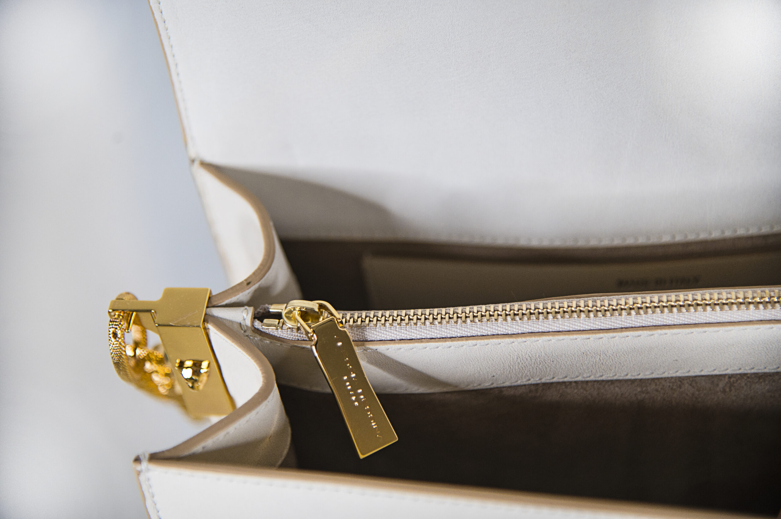 Close-up of a beige handbag zipper with gold accents.