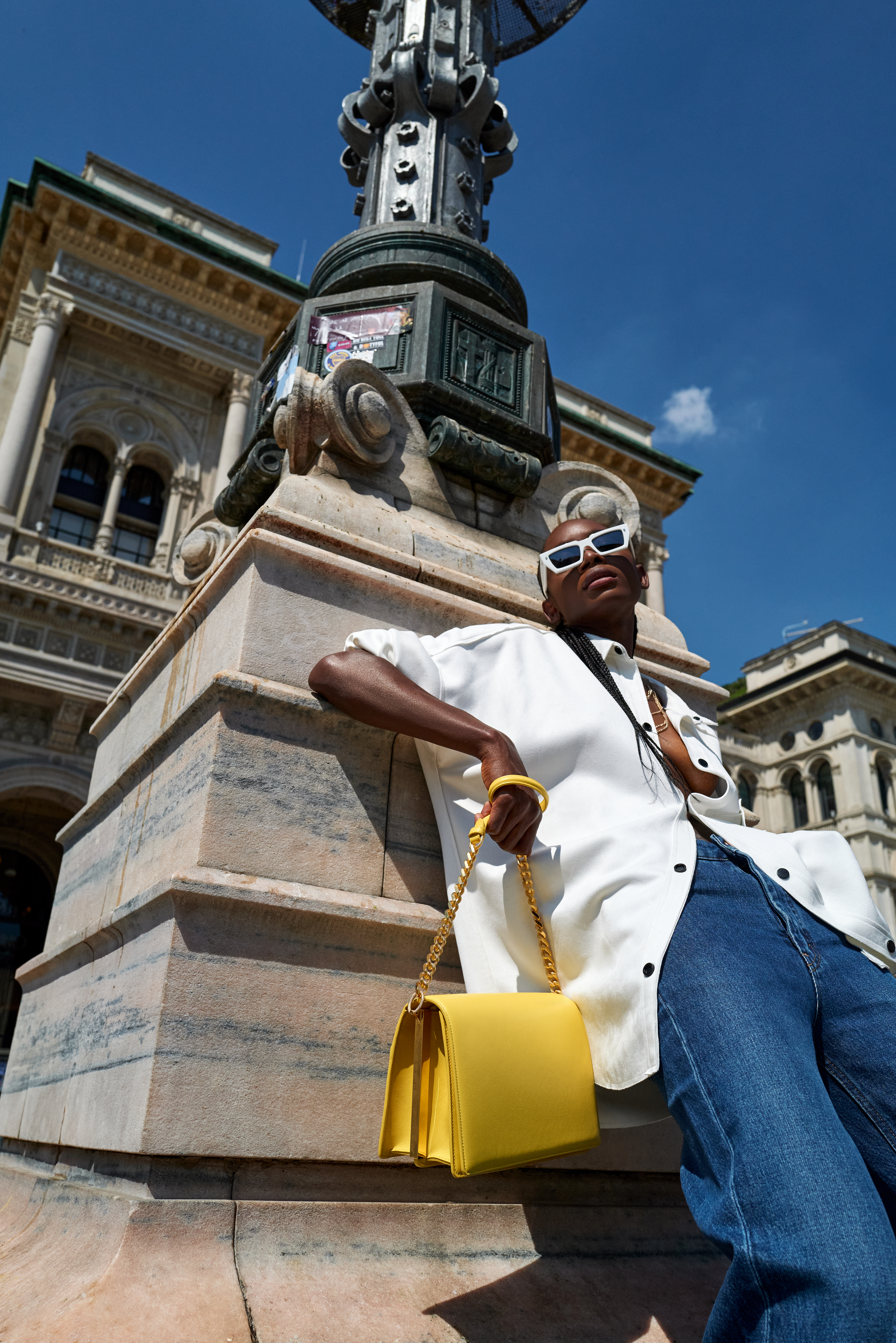 Fashionable person posing outdoors with a yellow bag and sunglasses.