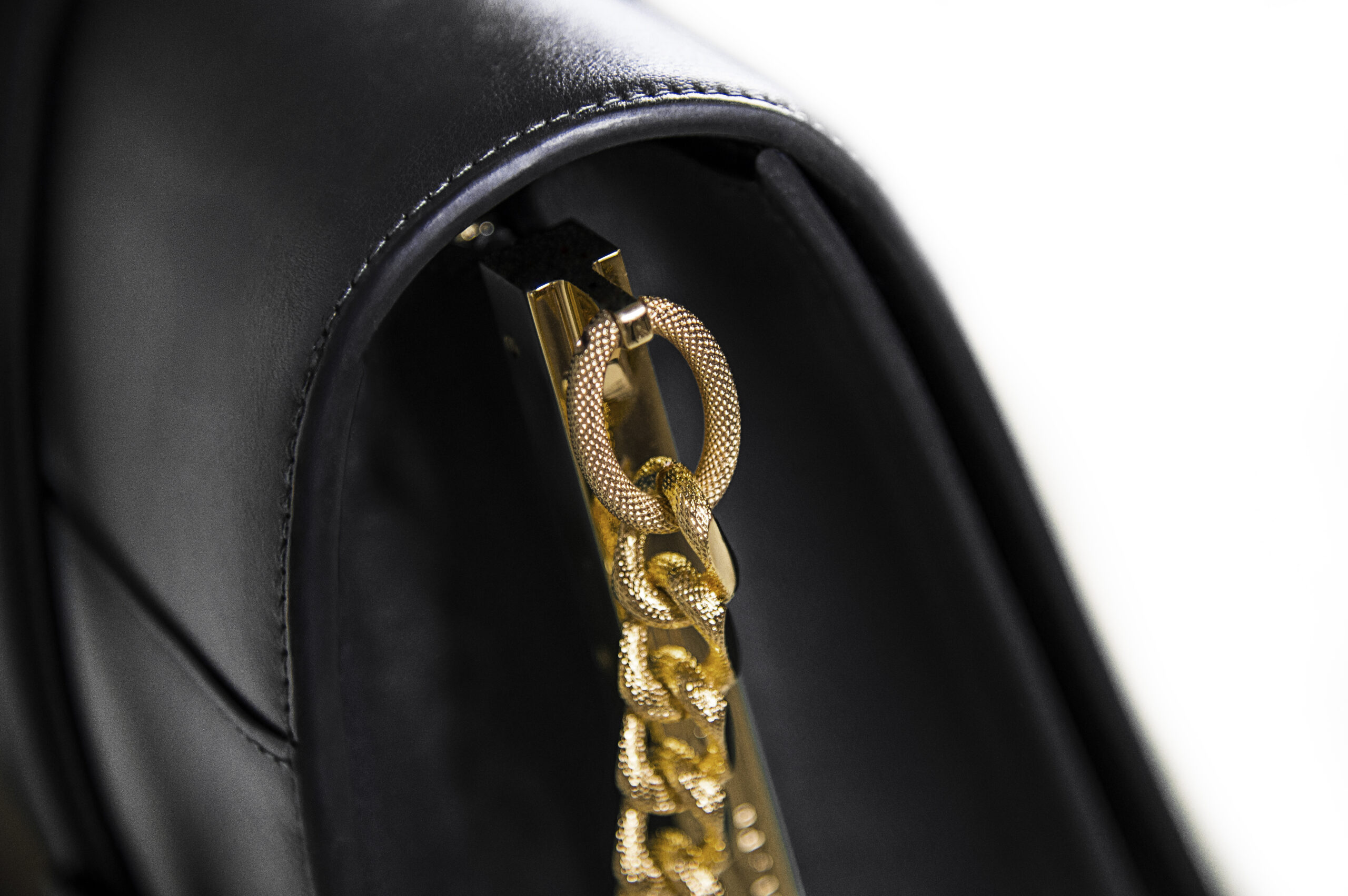 Close-up of a gold chain detail on a black leather accessory.
