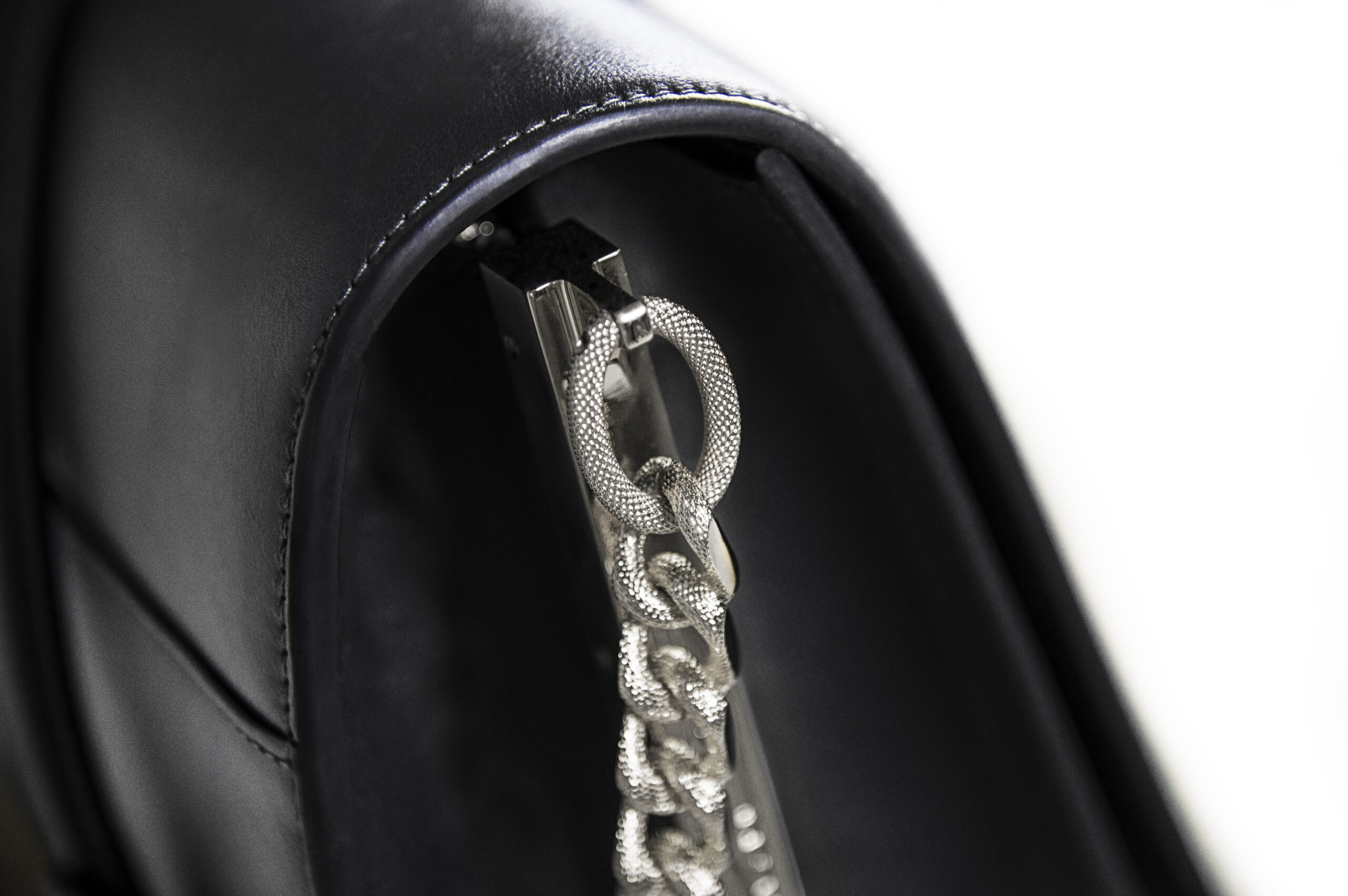 Close-up of a silver chain on a black leather bag.