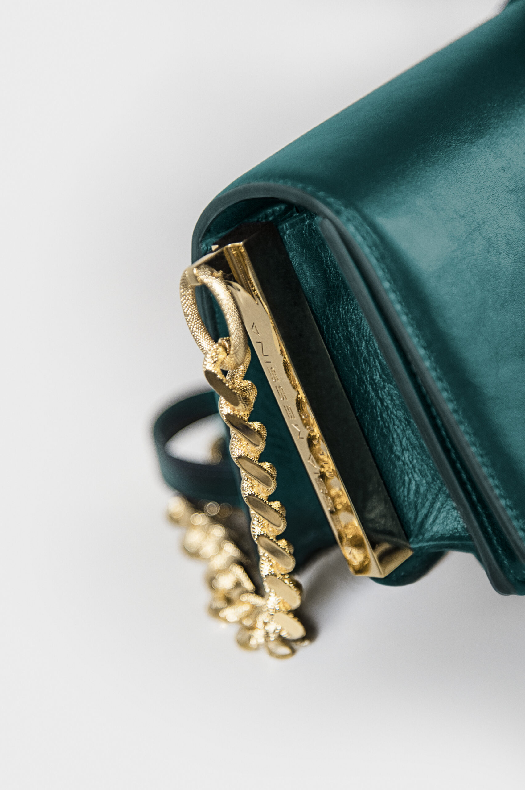 Close-up of a teal handbag with gold chain and zipper details.