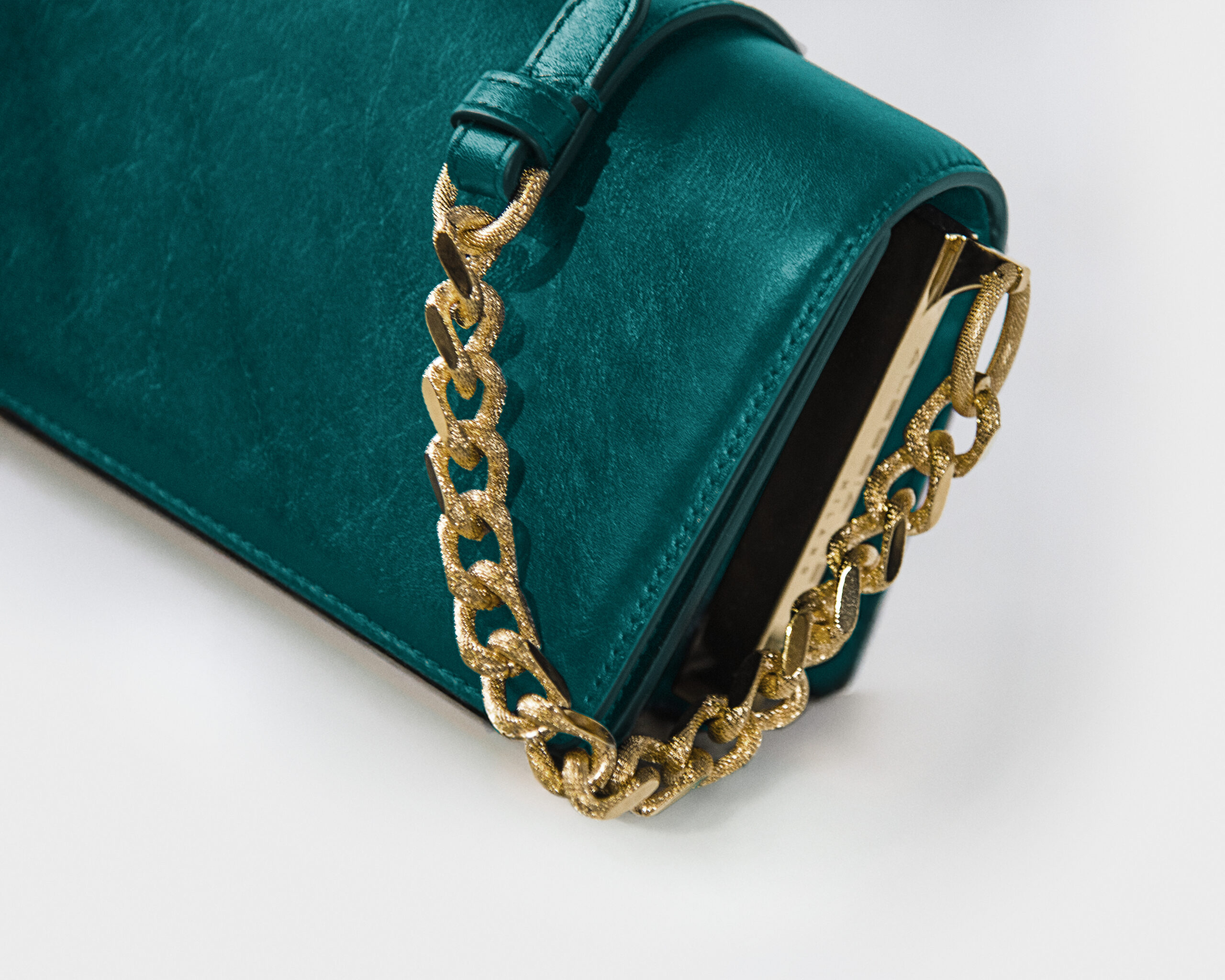 Close-up of a green velvet handbag with a gold chain strap.