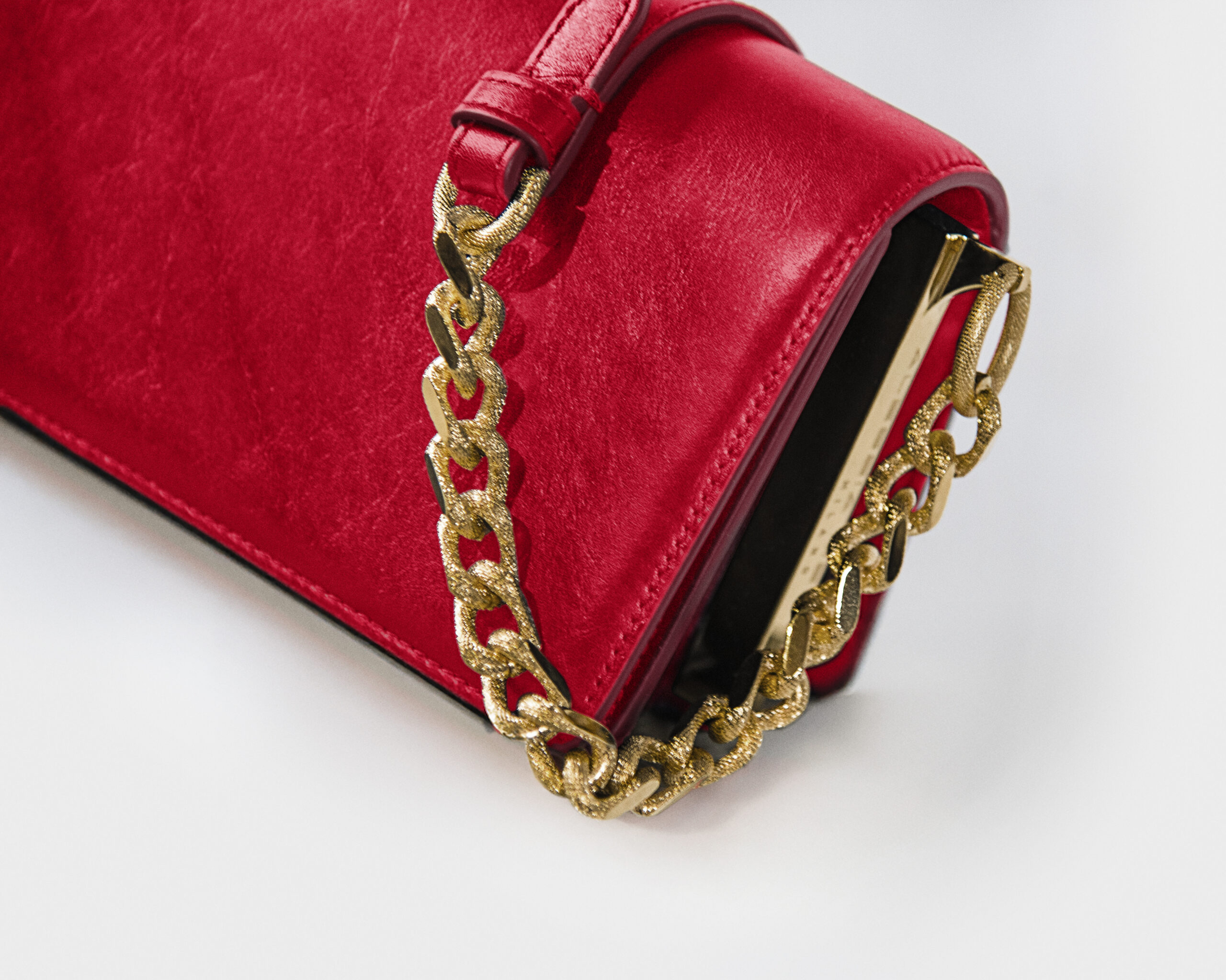 Close-up of a red suede handbag with a gold chain strap.