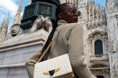 Woman posing stylishly near a historic cathedral with a luxury handbag.