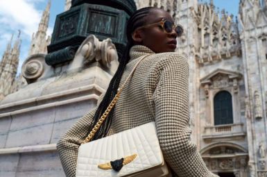 Woman posing stylishly near a historic cathedral with a luxury handbag.